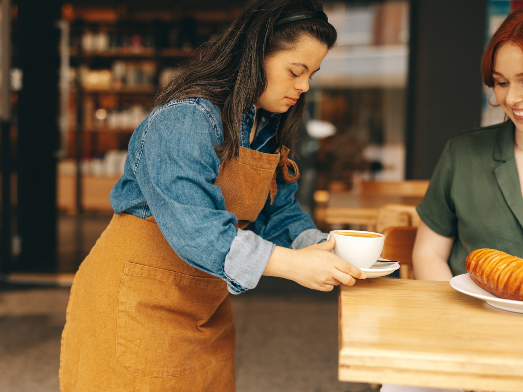 imagen de una mujer con síndrome de Down sirviendo un café a una clienta en una cafetería