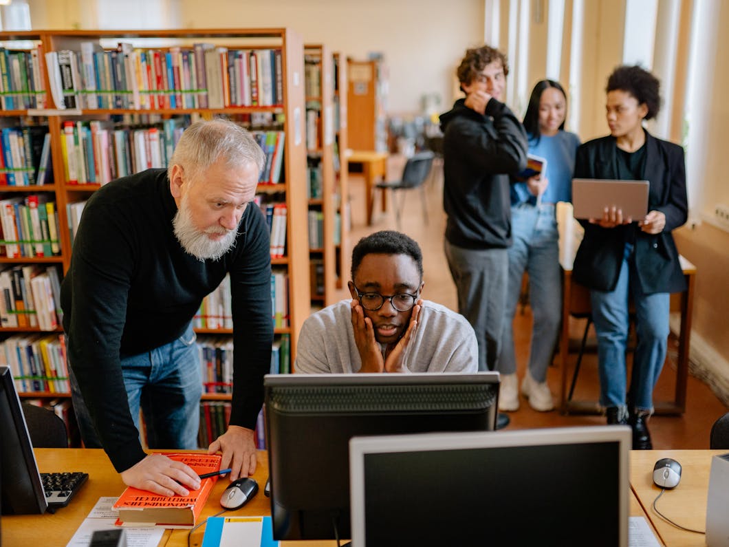 imagen de un grupo de personas en un centro educativo. Un profesor ayuda a un alumno junto a un ordenador