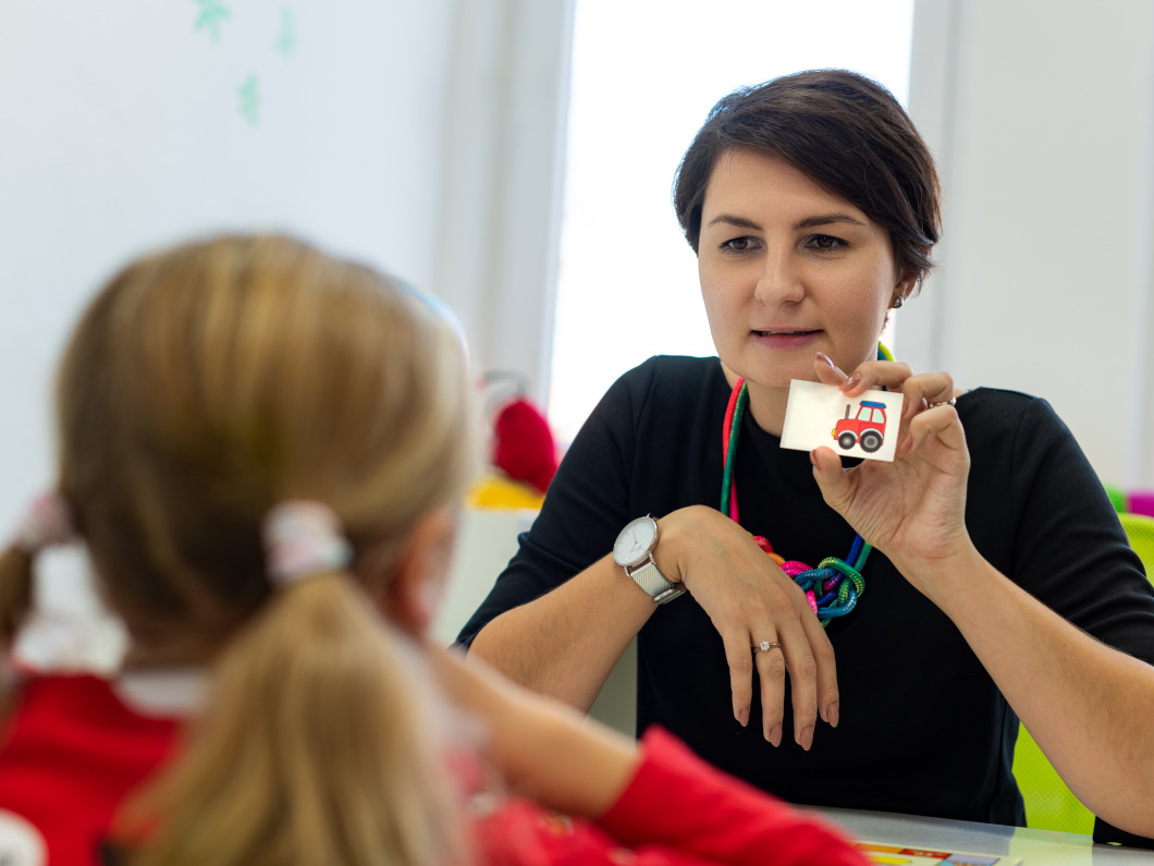 imagen de una docente enseñando una tarjeta con un pictograma a una niña que está sentada enfrente suya