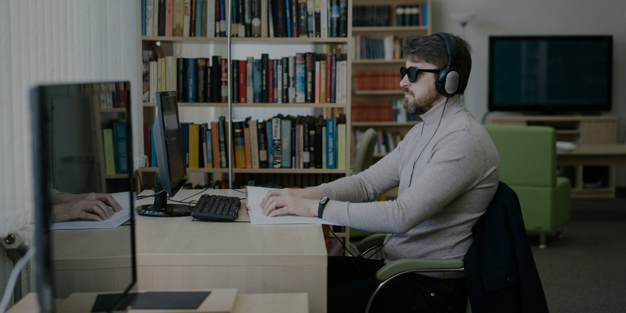 imagen de una persona ciega sentada en una mesa de escritorio mientras lee código braille