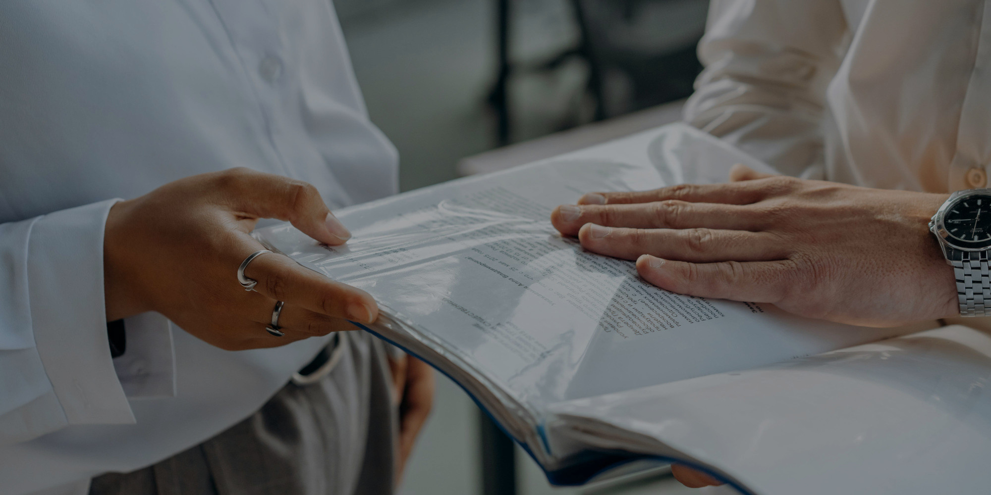 imagen detalle de las manos de varias personas señalando una carpeta con documentos