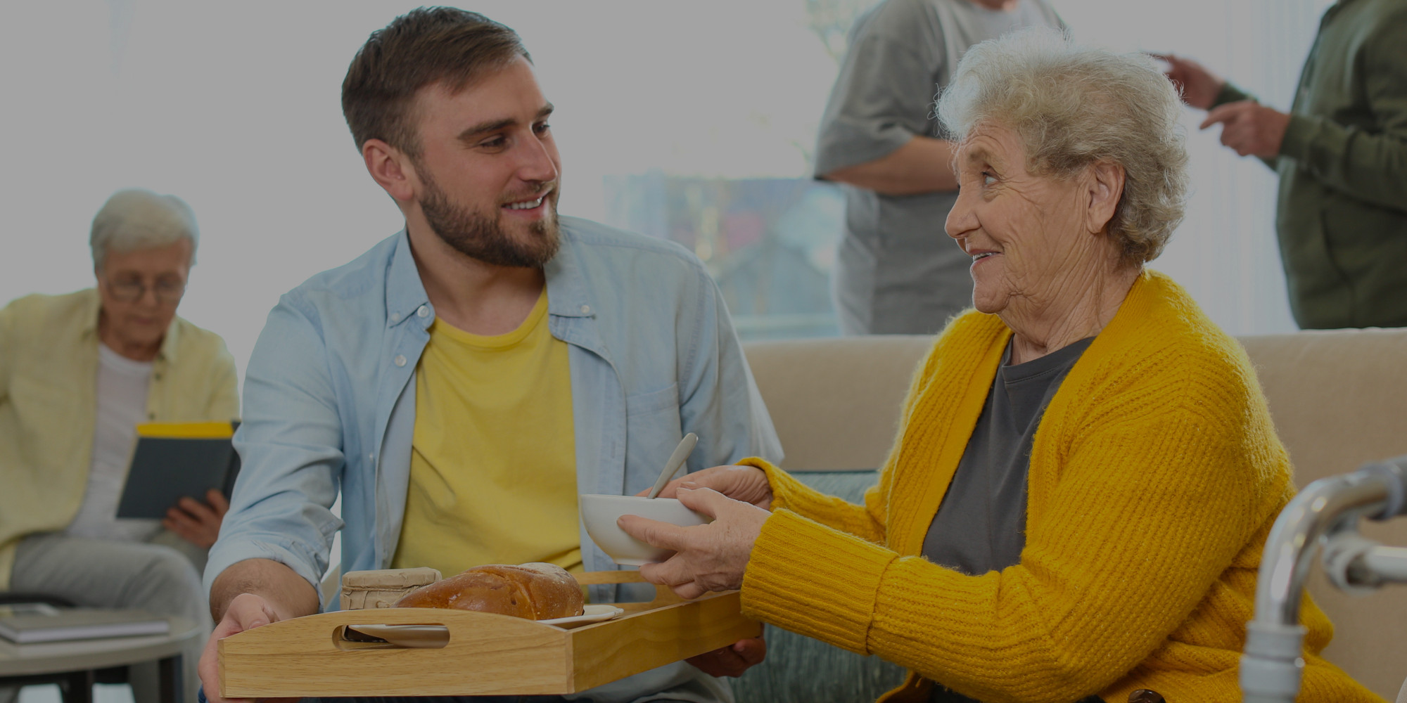 imagen de un joven ayudando a una mujer mayor a desayunar en una residencia